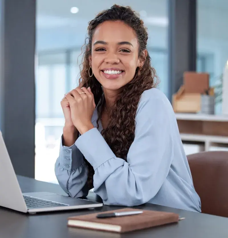 mulher jovem sorridente debruçada na mesa com laptop e agenda